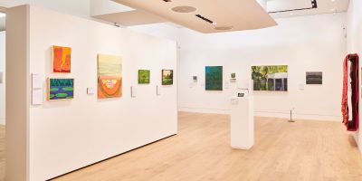 A white walled gallery space with several colourful landscape paintings hung up