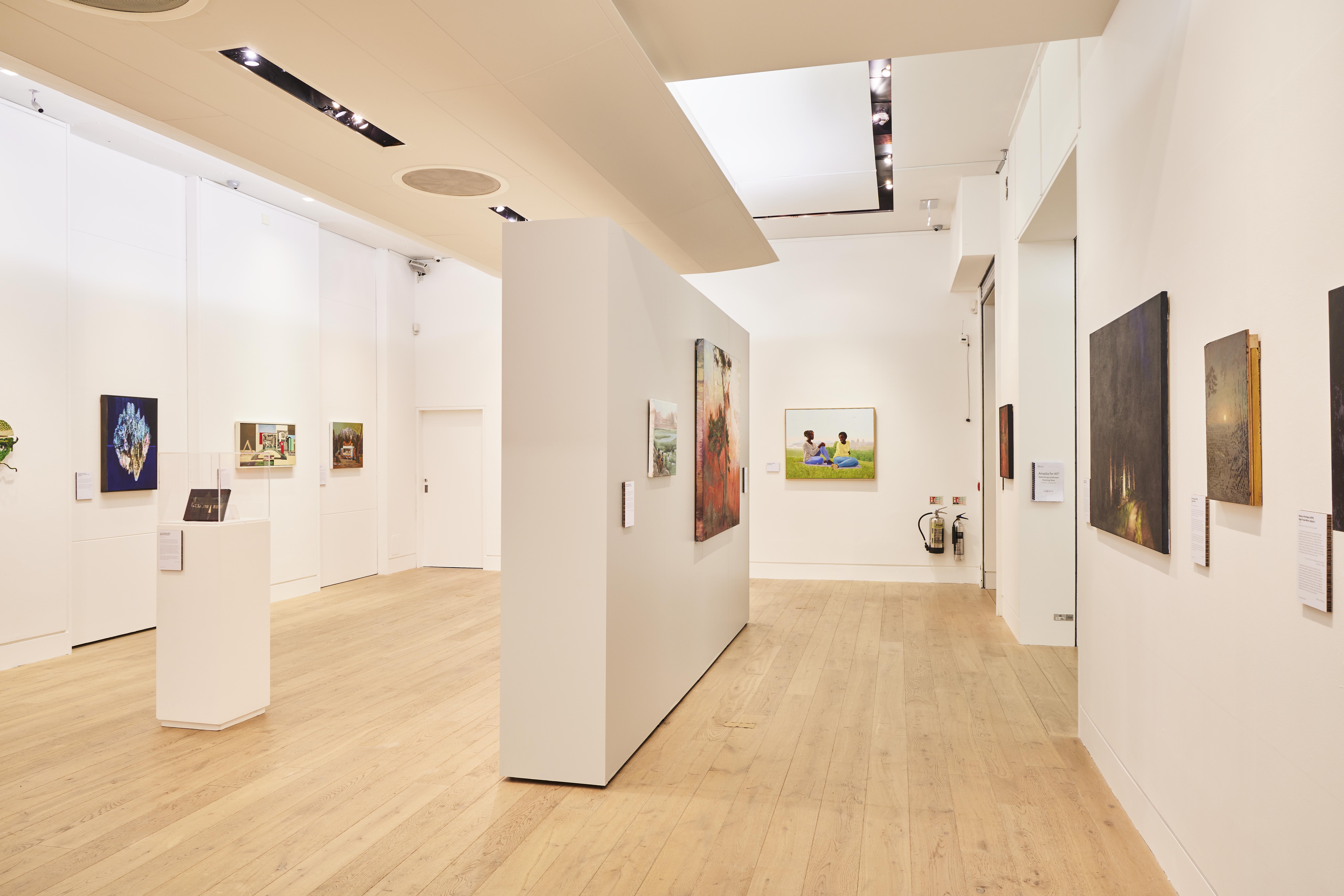 A gallery space with colourful landscape paintings hung on the walls